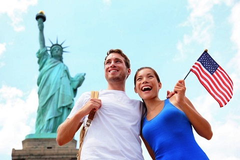 Pareja de turistas frente a la estatua de la libertad y con una bandera de USA en las manos